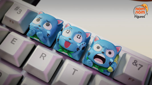 Close-up of Fairy Tail Happy keycaps on a keyboard, focusing on detailed facial expressions — the Shy Happy with blushing cheeks, the Cheerful Happy with a playful grin, and the Angry Happy shouting while holding a rolled scroll.