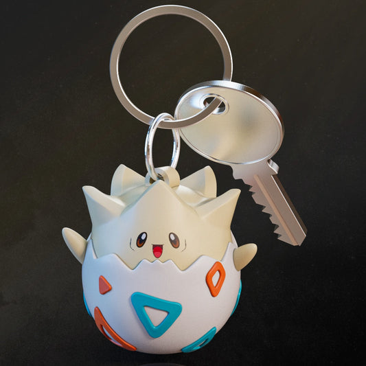 Togepi keychain with colorful eggshell design and smiling face, attached to metal keyring with a silver key – Pokémon collectible accessory.