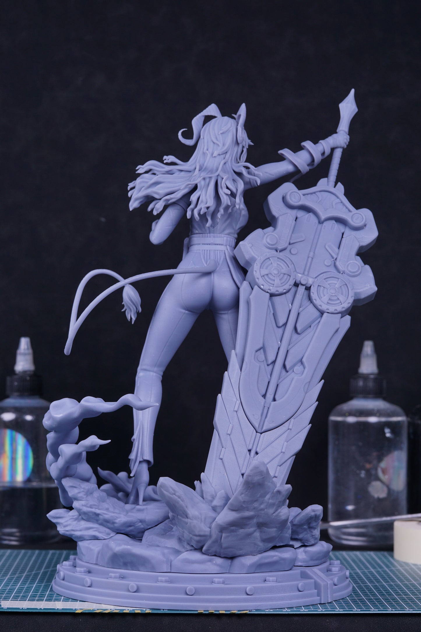 Rear view of gray resin figure showcasing the tail, sword detail, and wind-swept hair over a rocky display base.