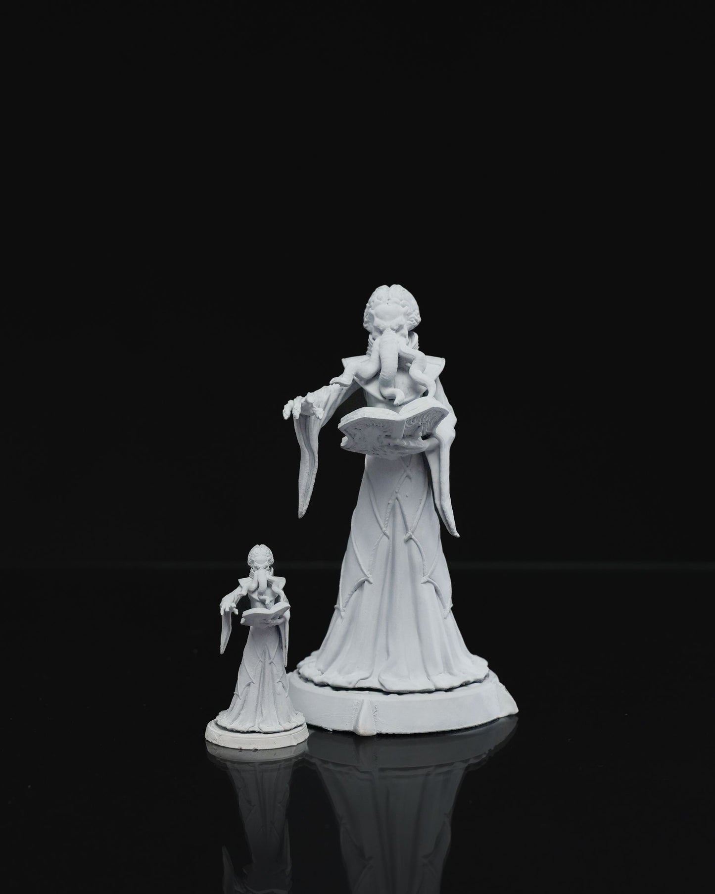 Mind Flayer miniature depicted reading a book with one hand, the other raised, tentacled face and dressed in a long gown, standing on a plain base.