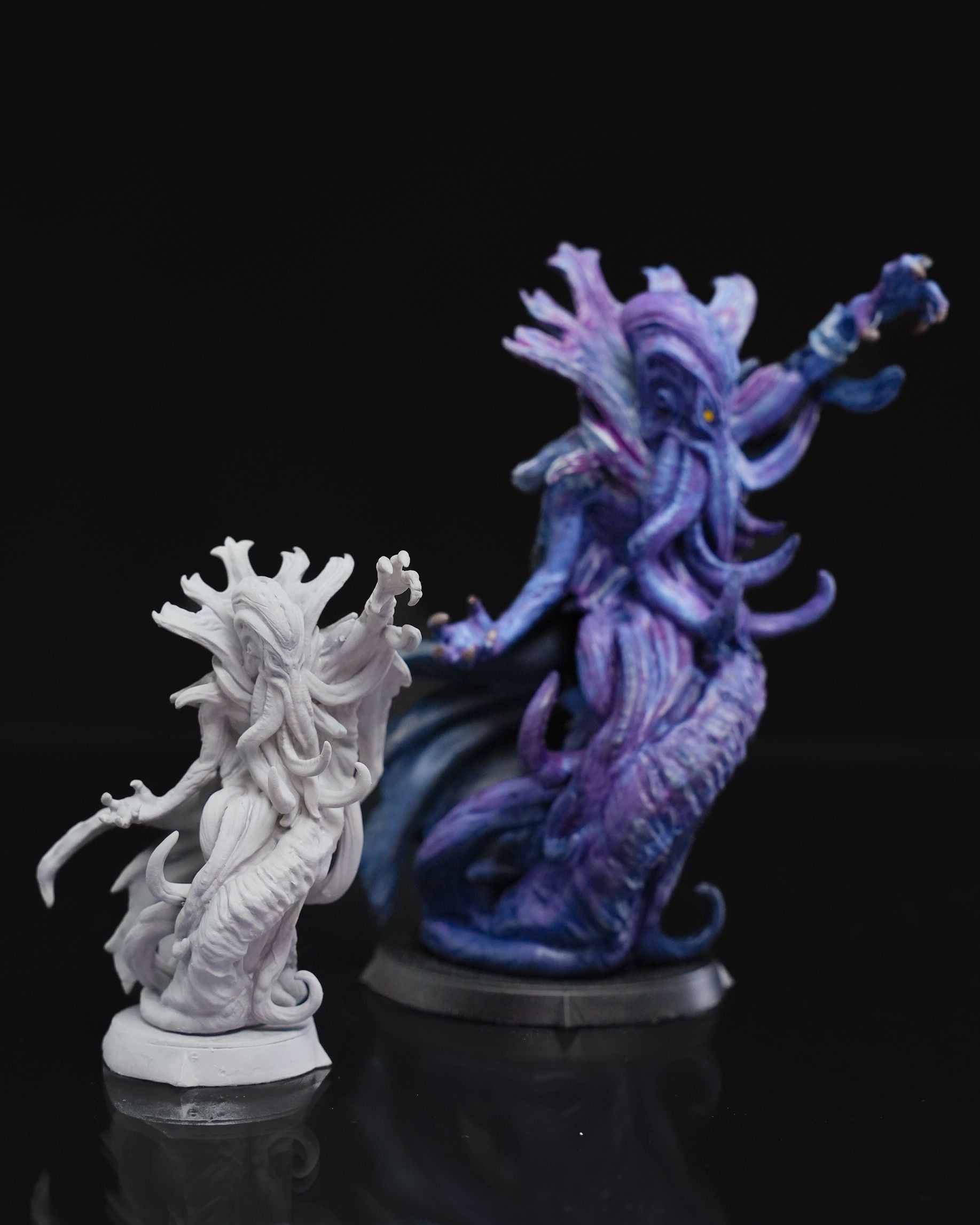 Two mind flayer miniatures side by side, one painted in vibrant purple and blue colors and the other unpainted in white, showcasing their details.