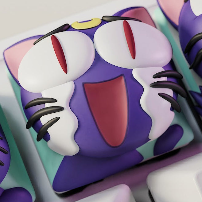 Close-up of the Laughing Luna keycap from Sailor Moon, showing the purple cat with closed eyes, wide mouth, and tear streaks of laughter, complete with her iconic crescent moon symbol.