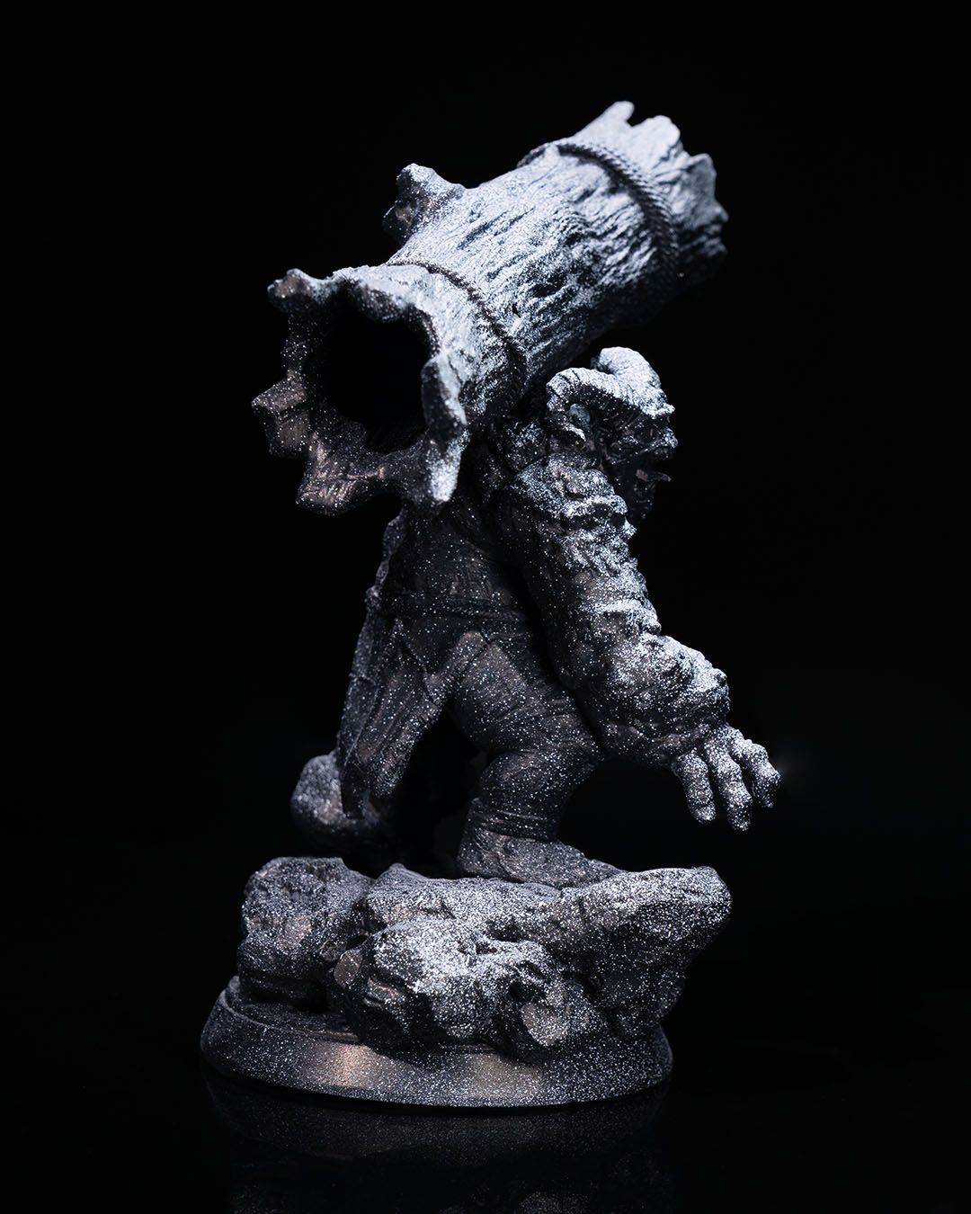 Side view of Orthos the Troll miniature, emphasizing the log's size and the troll's muscular build, standing on a textured base.