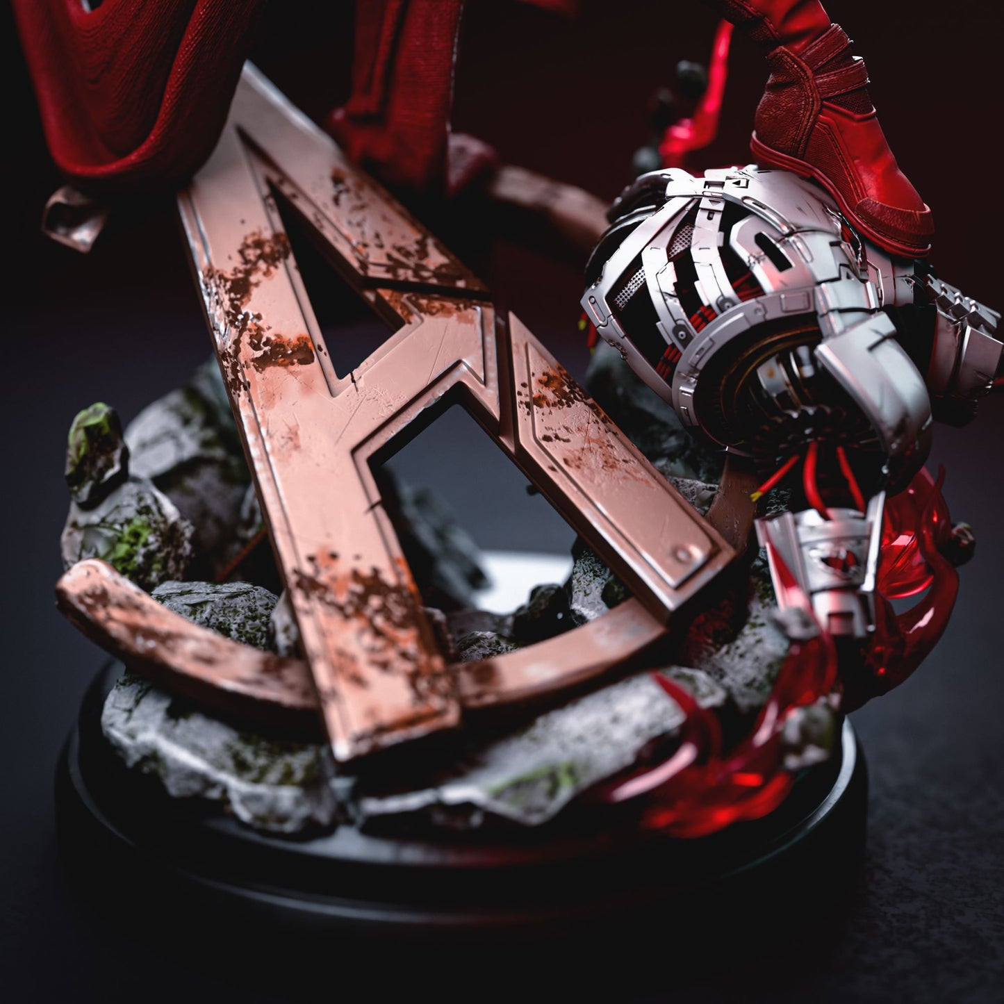 Base of Scarlet Witch figurine showing a weathered "A" symbol from the Avengers logo, with Ultron’s body beneath.