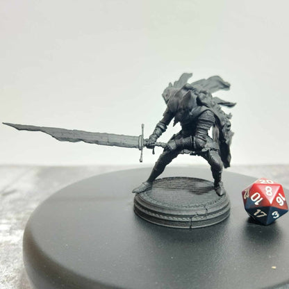 Red Hood (Slave Knight Gael inspired) miniature, cloaked warrior wielding a large sword, posed in a battle-ready stance with a flowing cape, next to a 20-sided dice.