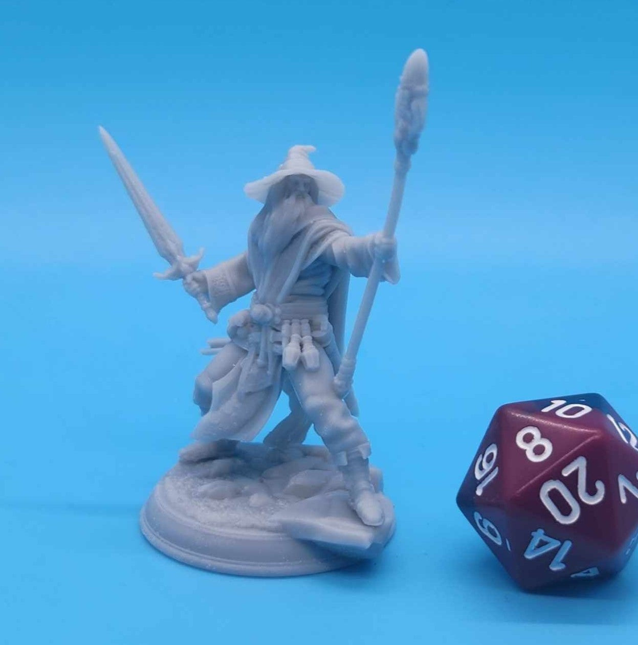 3D Printed Wizard Miniature with Staff and Sword Next to 20-sided Dice for Dungeons and Dragons (D&D), Pathfinder, Age of Sigmar, and Frostgrave.