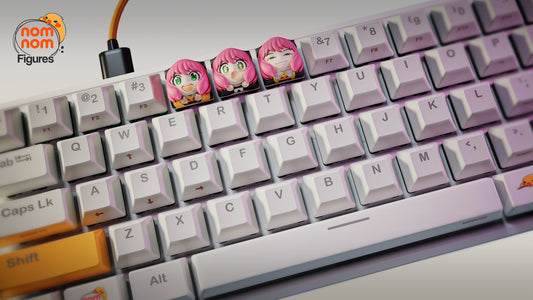 Full view of a mechanical keyboard featuring three Anya keycaps above the E, R, and T keys, showcasing vivid collectible keycaps against a white keyboard backdrop.