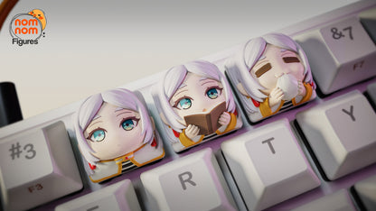 Close-up of three Frieren collectible keycaps inspired by Beyond Journey's End, featuring cheerful, sleepy, and serious chibi expressions, placed across the E, R, and T keys on a mechanical keyboard.