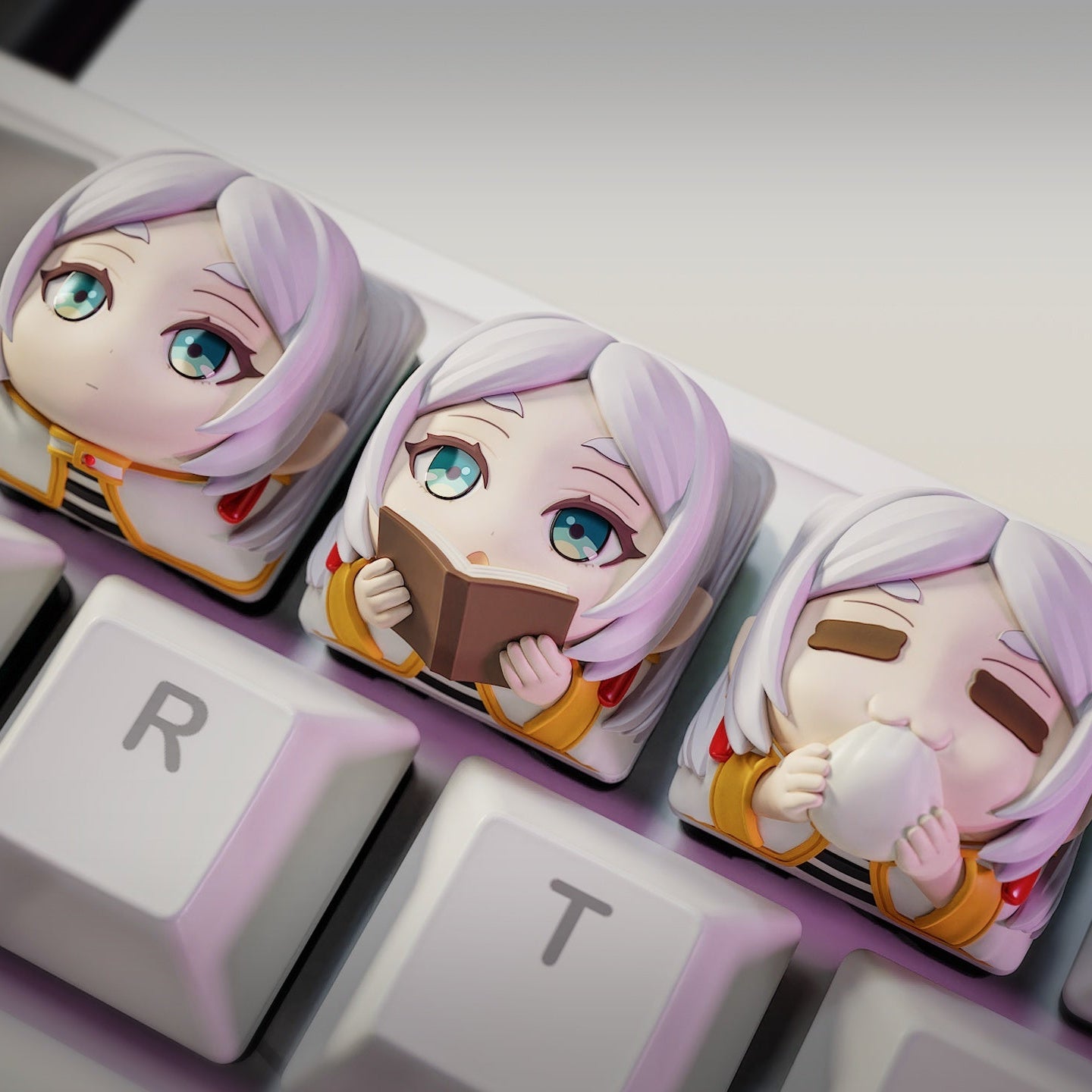 Top-down view of three Frieren keycaps with vibrant chibi expressions fitted to the E, R, and T keys, adding a playful and collectible look to the keyboard.