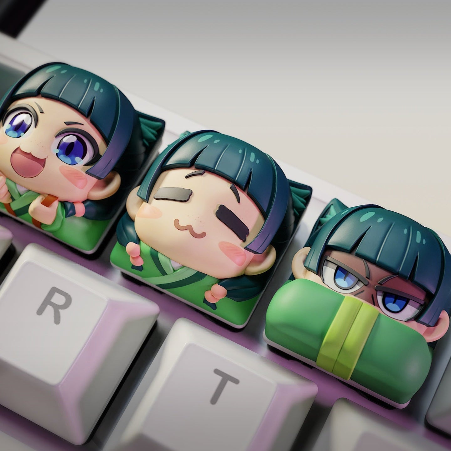 Top-down view of three Maomao keycaps with playful chibi expressions, fitted on the E, R, and T keys, showing bright, expressive faces for decorating keyboards.