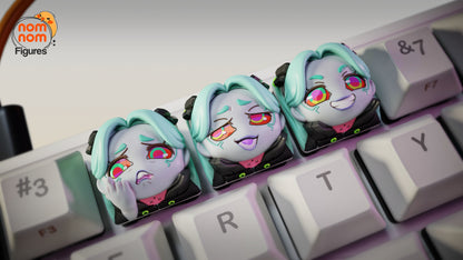 Close-up of three custom Rebecca keycaps from Cyberpunk: Edgerunners on a keyboard, showing sad, smug, and maniacal expressions.